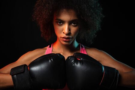 Image of young african american sportswoman working out in boxing gloves isolated over black backgroundの写真素材