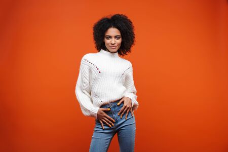 Beautiful smiling young african woman wearing sweater standing islolated over red background, posingの写真素材