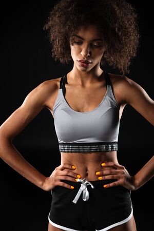 Image of young african american woman in sportswear posing with hands on waist isolated over black backgroundの写真素材