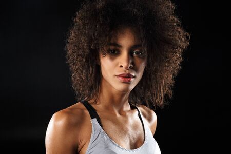 Image of athletic african american woman in sportswear posing and looking at camera isolated over black backgroundの写真素材