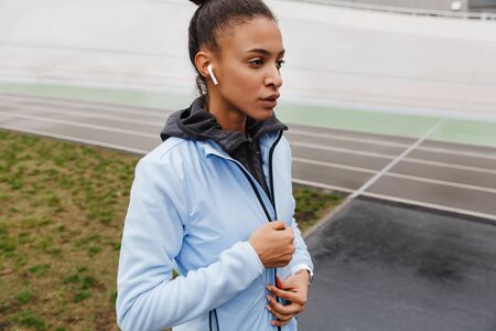 Attractive young healthy african sportswoman listening to music with wireless earphones wrking out...