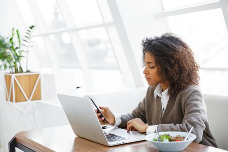 Portrait of young beautiful african american woman using laptop computer while having lunch in cafeの写真素材