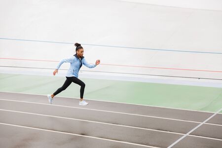Beautiful young fit african sportswoman wearing wireless earphones running at the stadium
