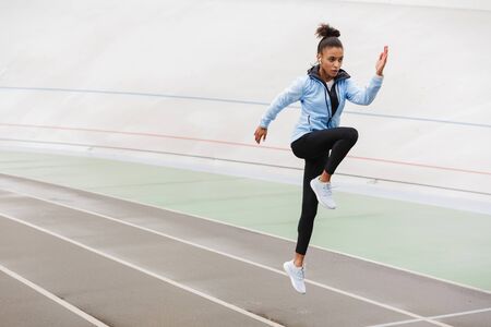 Beautiful young fit african sportswoman wearing wireless earphones doing stretching exercises at the...