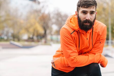 Attractive young tired sportsman resting after jogging outdoorsの写真素材