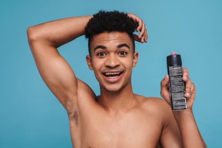Photo of excited african american man showing his armpit and deodorant spray isolated over blue backgroundの写真素材