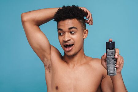Photo of excited african american man showing his armpit and deodorant spray isolated over blue backgroundの写真素材