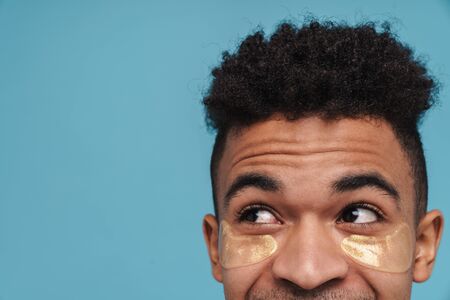 Cropped photo of african american man with under eye patches looking upward isolated over blue backgroundの写真素材
