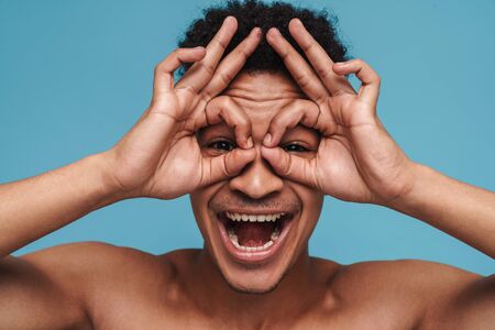 Photo of funny african american man grimacing with his fingers isolated over blue background