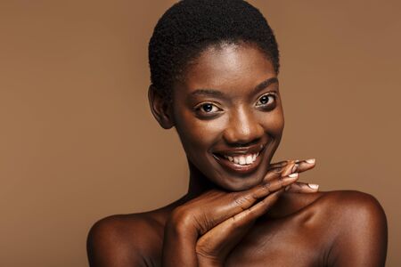 Beauty portrait of attractive young half-naked african woman with short black hair isolated over beige backgroundの写真素材