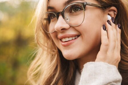 Close up of a beautiful young cheerful woman wearing coat walking in the autumn park, wearing...