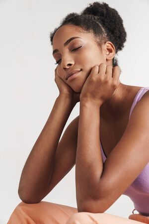 Portrait of african american calm woman sitting with eyes closed isolated over white backgroundの写真素材
