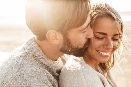 Close up of a smiling beautiful young couple embracing while standing at the beachの写真素材