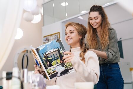 Image of a young beautiful amazing blonde girl indoors in beauty salon with hairdresser reading...