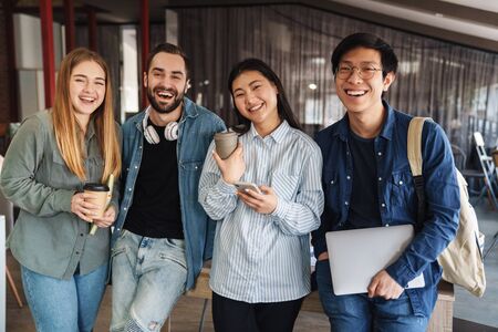 Photo of multinational cheerful students laughing and looking at camera while standing in classroom