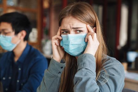 Photo of caucasian young student with headache in medical masks studying at classroomの写真素材
