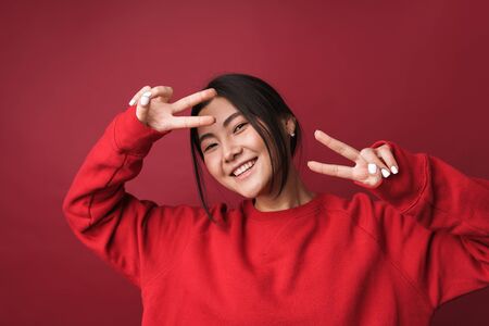 Close up of a pretty smiling young asian woman wearing casual clothes standing isolated over red...