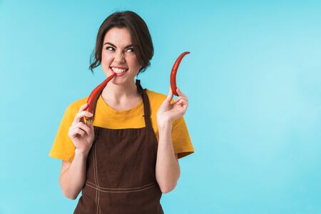 Image of young beautiful woman chef holding chili pepper isolated over blue wall background.の写真素材