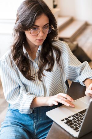 Attractive pensive young brunette woman studying in the cafe indoors, working on laptop computerの写真素材