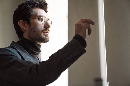 Image of handsome unshaven young businessman wearing suit holding and writing with marker in cafe
