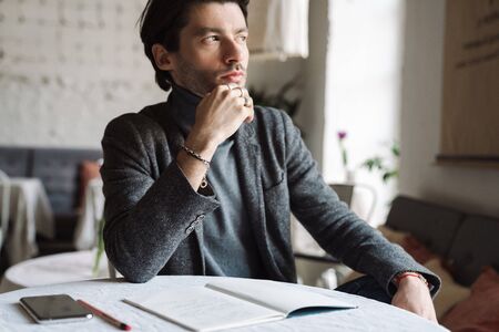 Close up of a handsome young bearded man wearing turtleneck sitting at the cafe, workingの写真素材