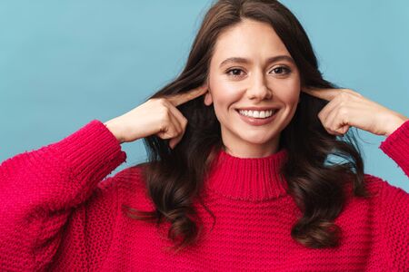 Photo of caucasian happy woman smiling at camera and plugging her ears with fingers isolated over blue backgroundの写真素材