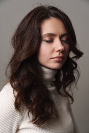Photo of caucasian young woman having long brown hair standing with eyes closed isolated over beige backgroundの写真素材