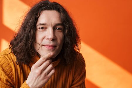 Image closeup of pleased young man posing and looking at camera isolated over orange wall with lightの写真素材