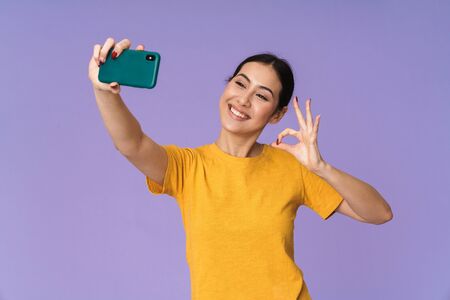 Cheerful young pretty sportswoman standing isolated over violet background, taking a selfie, showing...