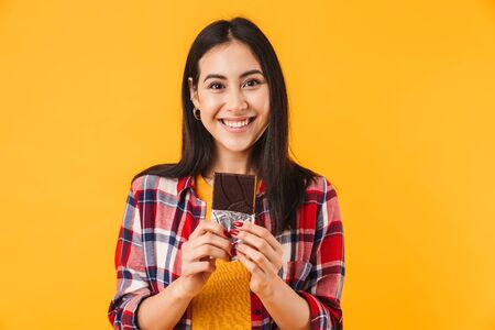 Image of cheerful caucasian woman smiling and holding chocolate isolated over yellow background
