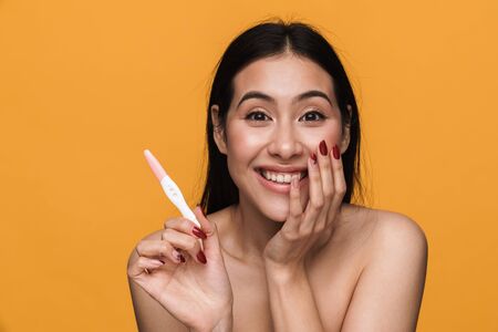 Beauty portrait of young half-naked woman rejoicing while holding pregnancy test isolated over yellow backgroundの写真素材