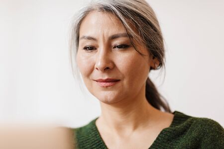 Image of concentrated mature beautiful grey-haired woman using laptop computer indoors.