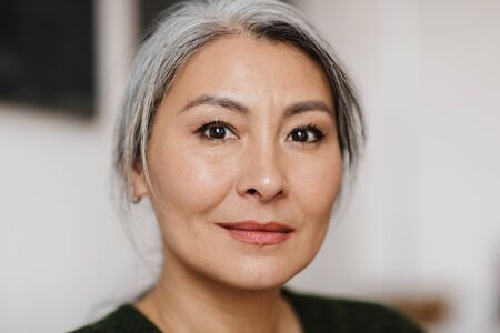 Photo closeup of gray-haired beautiful woman posing and looking at camera in living room