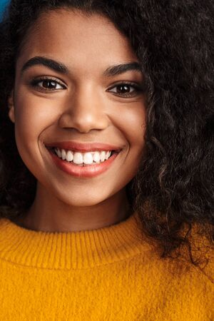 Closeup image of a beautiful smiling optimistic young african woman posing isolated over blue wall...