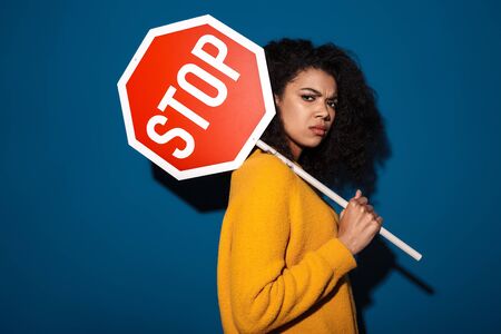 Photo of a pretty serious african woman posing isolated over blue wall background holding stop symbol sign.の写真素材