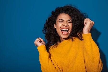 Image of a pretty young excited screaming african woman posing isolated over blue wall background.の写真素材