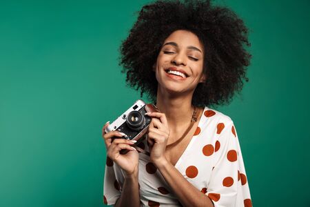Portrait of a happy young african woman standing isolated over green background, wearing summer clothes, holding photo cameraの写真素材