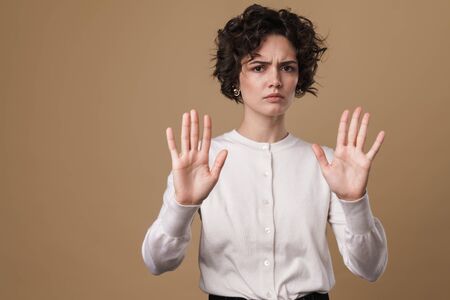 Image of displeased young woman showing stop gesture at camera isolated over beige background