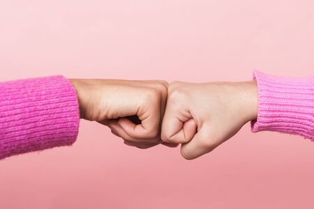 Image closeup of two teenage girls bumping their fists together in conciliation or friendship isolated over pink backgroundの写真素材