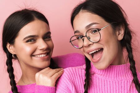 Image of two happy teenage girls with braids in casual clothes smiling at camera isolated over pink backgroundの写真素材