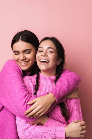 Two cheerful cute teenage girls having fun isolated over pink background, grimacing, huggingの写真素材