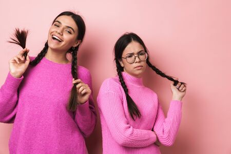Image of two young teenage girls with good and bad mood posing at camera isolated over pink...