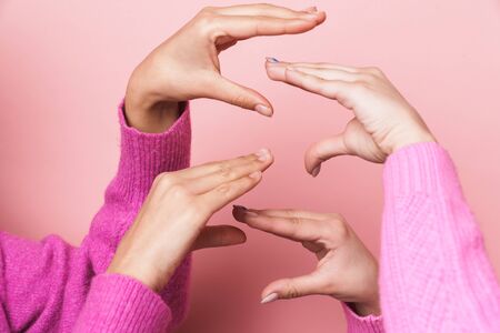 Image closeup of two teenage girls playing together and making figures with hands isolated over pink backgroundの写真素材