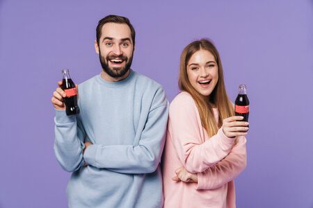 Photo of a cheery happy loving couple friends isolated over purple wall background drinking soda.