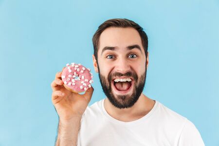 Photo of young screaming happy positive man isolated over blue wall background with donut.
