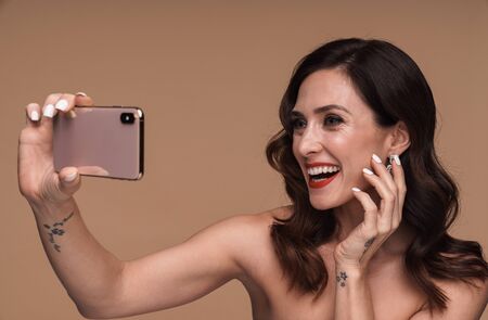 Beauty portrait of happy gorgeous adult half-naked woman smiling and holding cellphone isolated over...