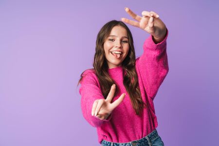 Image of young beautiful woman with long brown hair smiling and gesturing peace fingers isolated over violet backgroundの写真素材