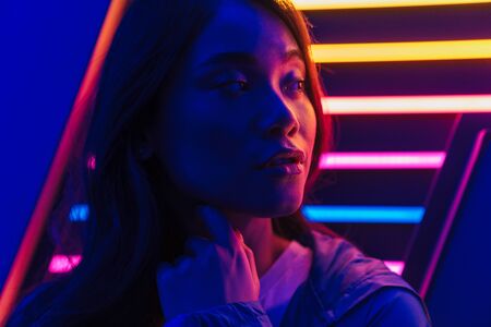Beautiful young asian woman with long dark hair standing infront of a neon wall, posingの写真素材
