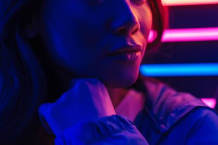 Cropped image of a beautiful young asian woman with long dark hair standing infront of a neon wallの写真素材
