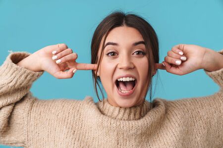 Image of delighted young woman smiling and plugging her ears isolated over blue background